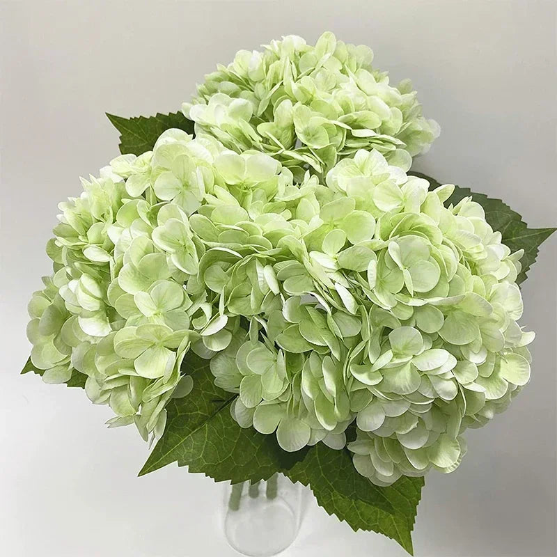A bouquet of large artificial lime green hydrangea flowers with dark green leaves.