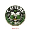 A round green coin featuring a silhouette of a beer mug and laurel leaves with the text Cheers and Fckers.