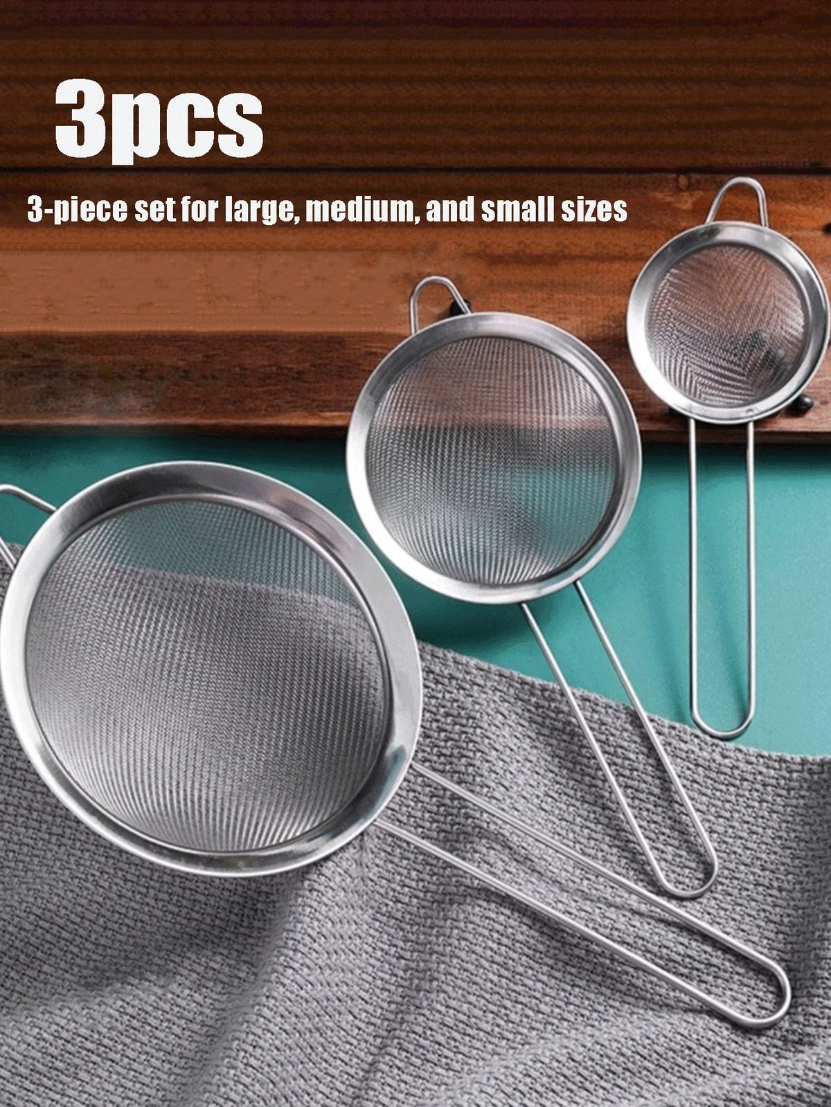 A set of three stainless steel colanders and strainers are displayed on a wooden surface and a gray cloth.