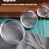 A set of three stainless steel colanders and strainers are displayed on a wooden surface and a gray cloth.