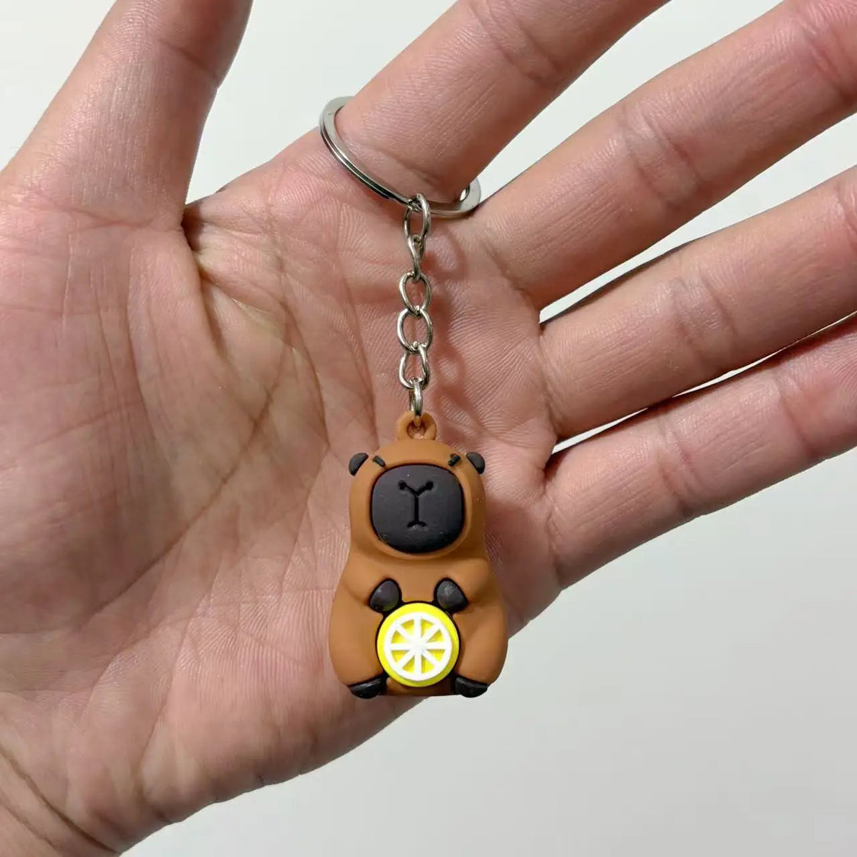 Un petit pendentif de clé USB de capybara brun avec un détail de roue jaune est tenu dans la main d'une personne.