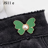 A close-up of a green butterfly button with a pearl center attached to black denim fabric.