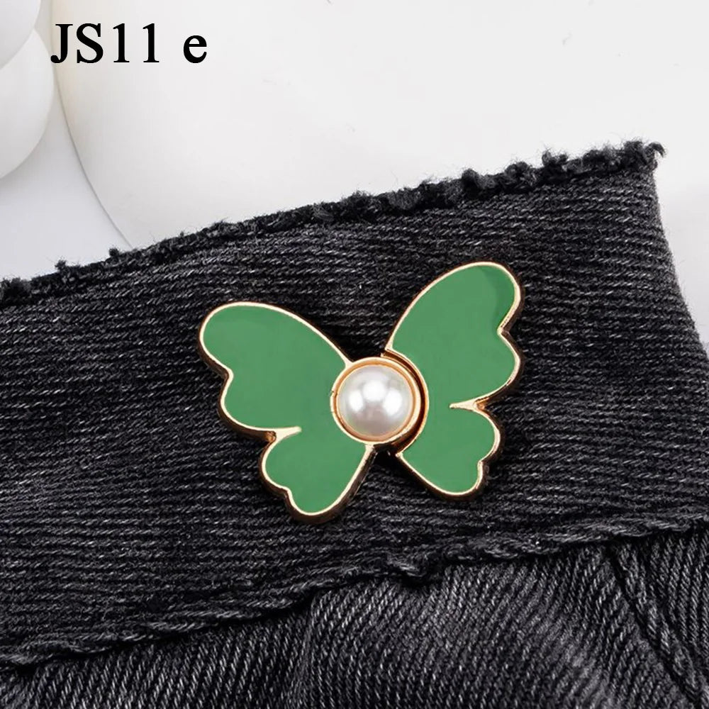 A close-up of a green butterfly button with a pearl center attached to black denim fabric.