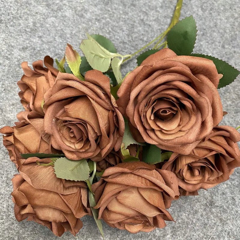 A bouquet of nine realistic silk roses in various shades of brown and copper on a gray background.