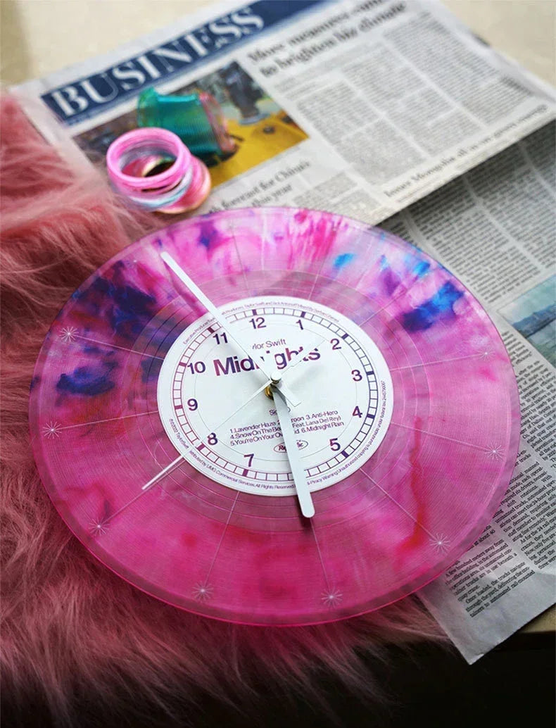 A pink and purple marbled vintage vinyl record wall clock with a white face is displayed on a surface next to a newspaper.