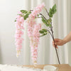 A branch of pink artificial wisteria hanging vine with silk blooms and green leaves