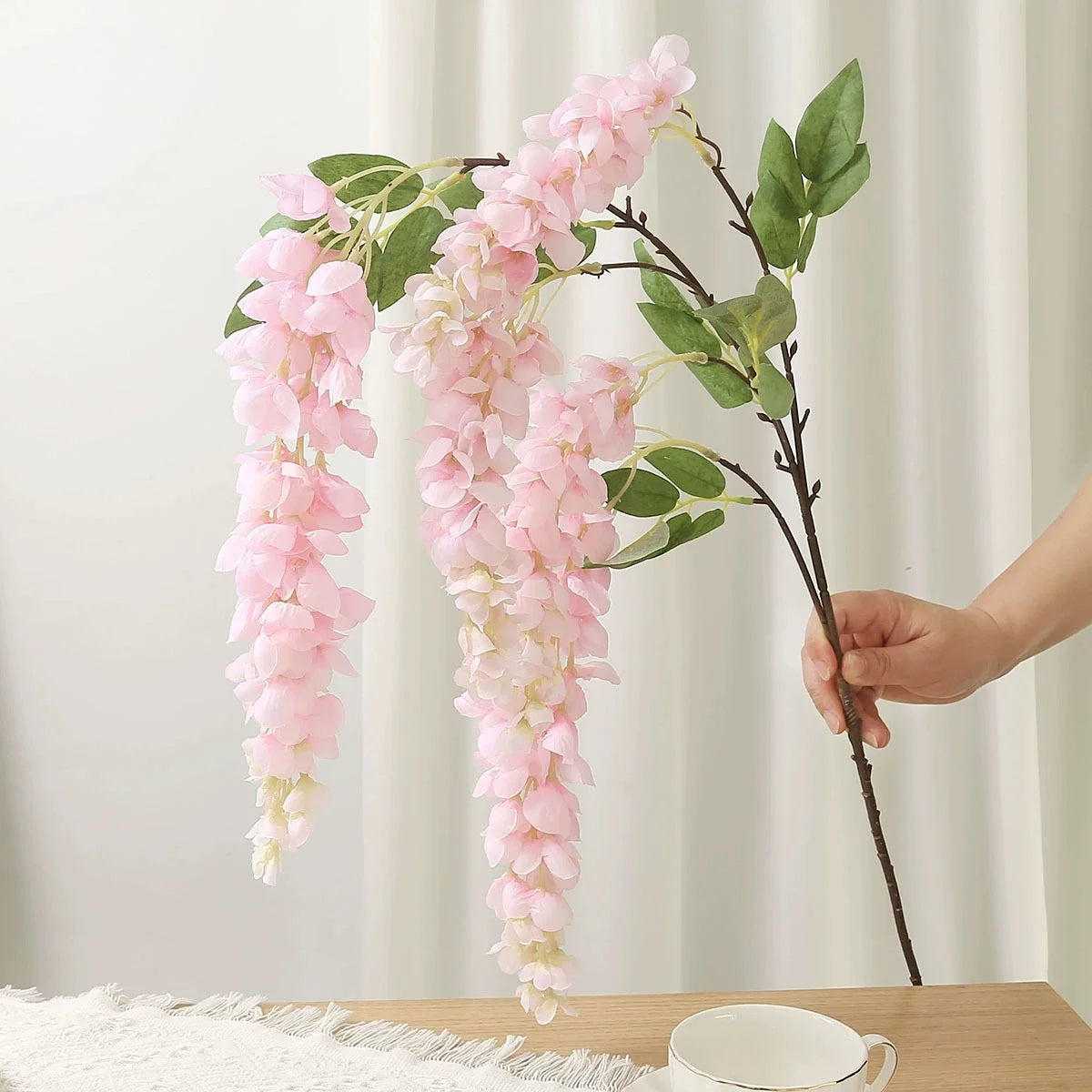 A branch of pink artificial wisteria hanging vine with silk blooms and green leaves