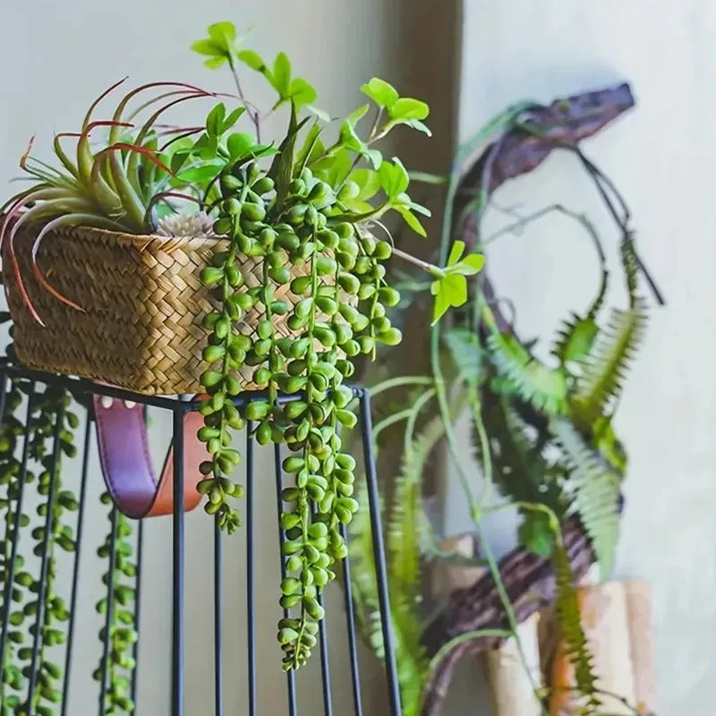 Artificial hanging succulent vine with green leaves and stems displayed in a black hanging planter.