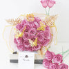 A bouquet of pink and purple glitter artificial roses with gold crowns and gold butterflies displayed in elegant packaging.