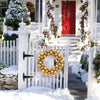 A golden silk Christmas ball wreath ornament displayed on a white picket fence in a snowy outdoor setting.