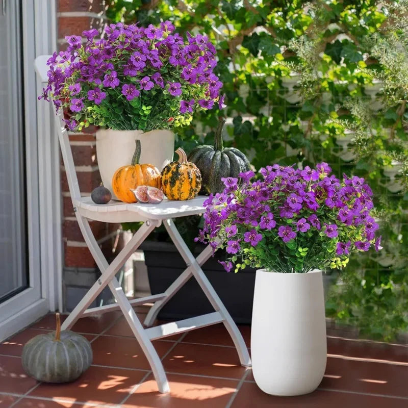 A white folding stand holds a large purple flower arrangement and several pumpkins in front of a green garden backdrop.