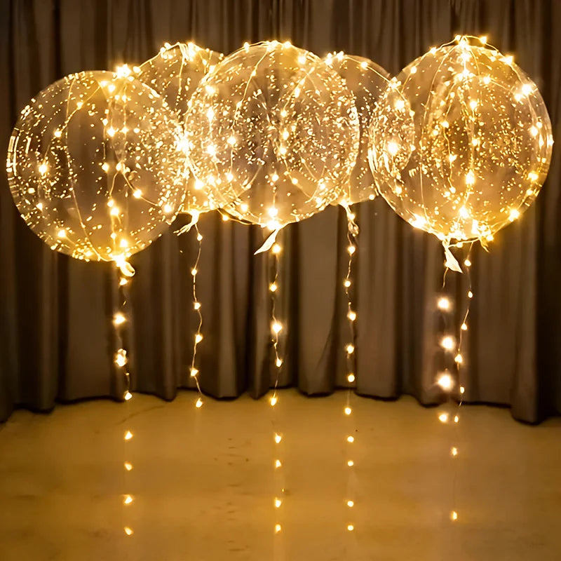 A cluster of transparent LED light-up balloons with warm glow string lights hanging against a dark curtain.