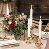 A floral arrangement featuring deep red and pink roses and greenery, set on a table with white candles.