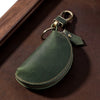 A dark olive green Crazy Horse leather key pouch with a brass carabiner attached, resting on a brown surface.