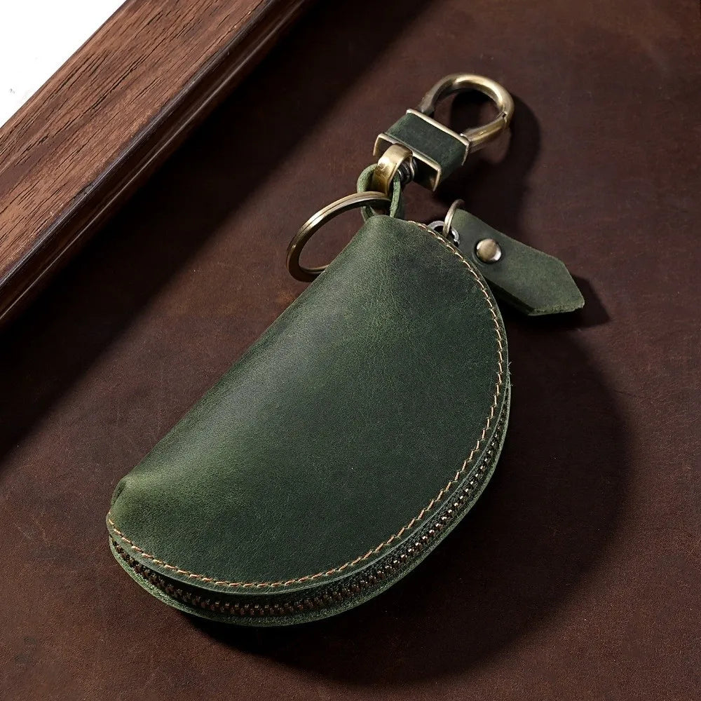 A dark olive green Crazy Horse leather key pouch with a brass carabiner attached, resting on a brown surface.