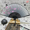 An elegant vintage Chinese folding hand fan with pink floral designs rests on a bamboo stand.