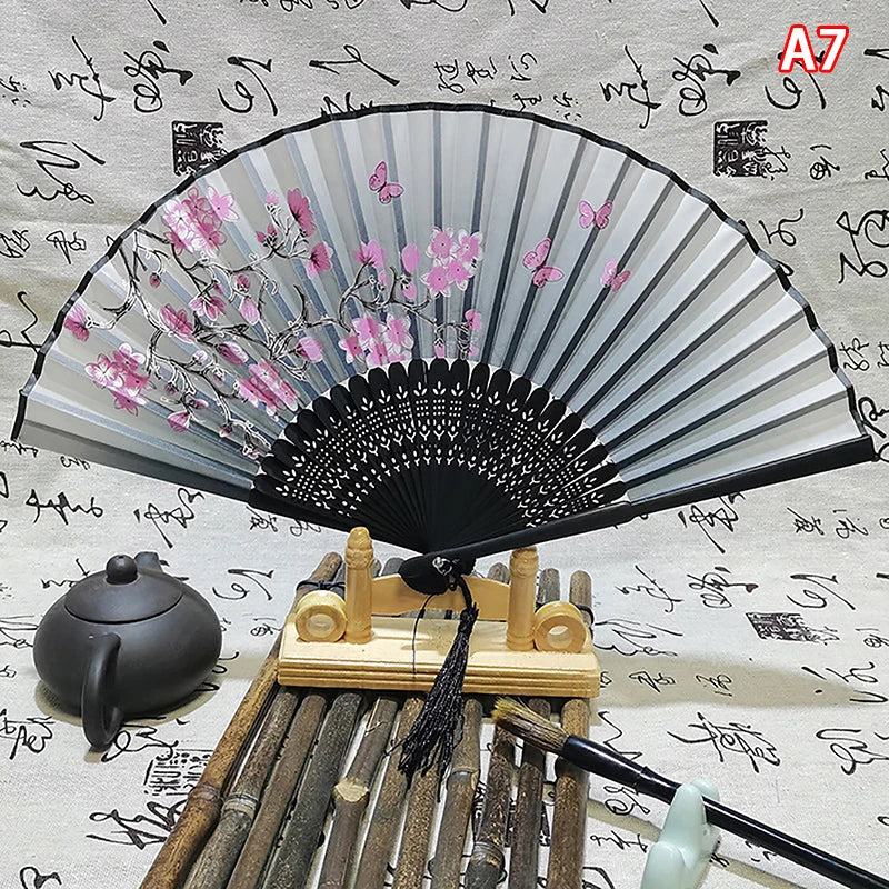 An elegant vintage Chinese folding hand fan with pink floral designs rests on a bamboo stand.