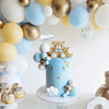 A tiered blue cake decorated with a bear topper and star accents, surrounded by various balloons.