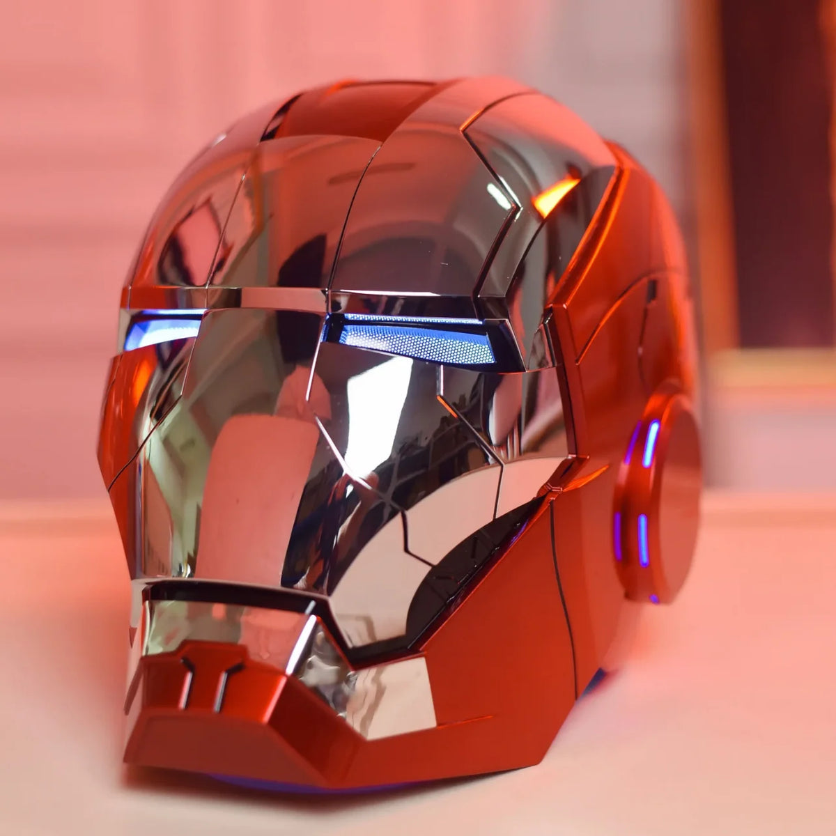 A metallic orange Iron Man MK5 wearable helmet with blue LED lights displayed on a surface.