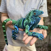 A hand holds a green articulated 3D printed lizard figurine for home decor.