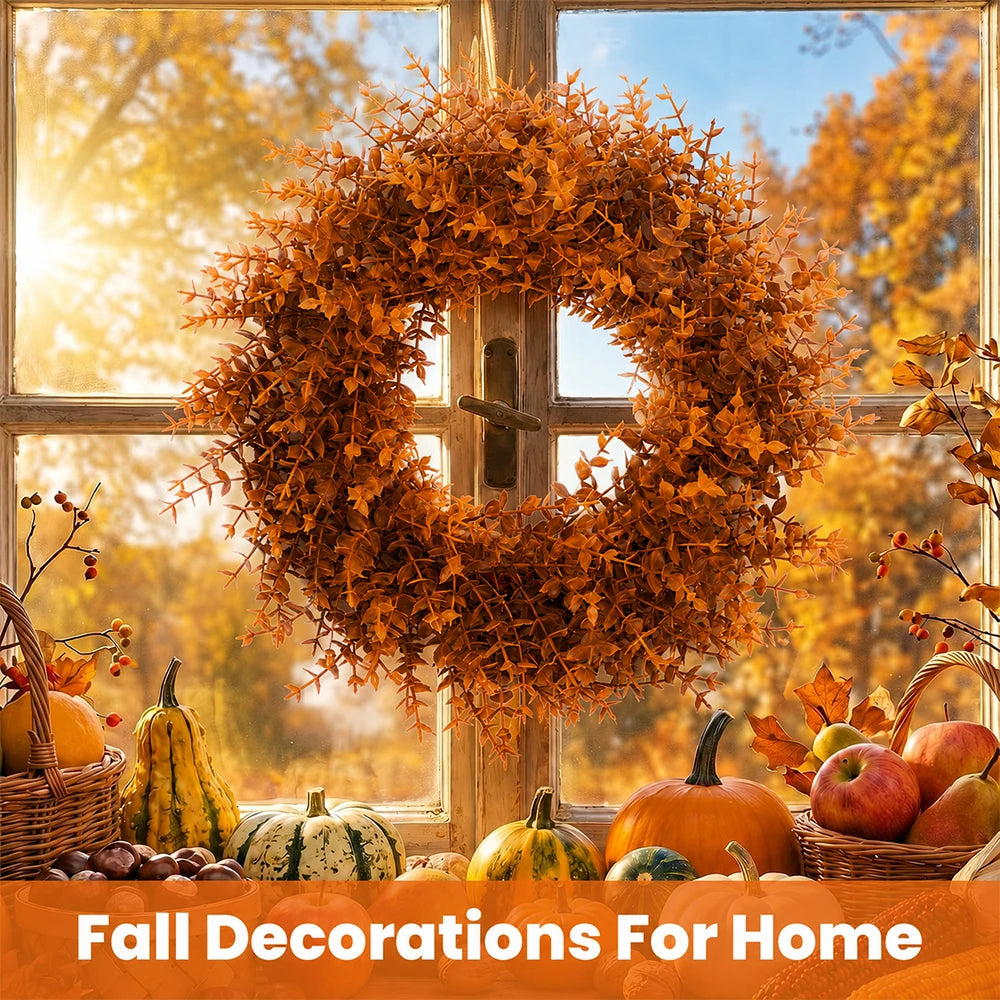 An artificial autumn wreath made of dried orange leaves hangs in front of a window with fall harvest decorations.