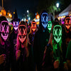 Group of people wearing glow-in-the-dark LED purge masks for Halloween cosplay at a night event