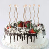 A white cake decorated with chocolate drip and cream frosting, topped with several tall, thin candles.