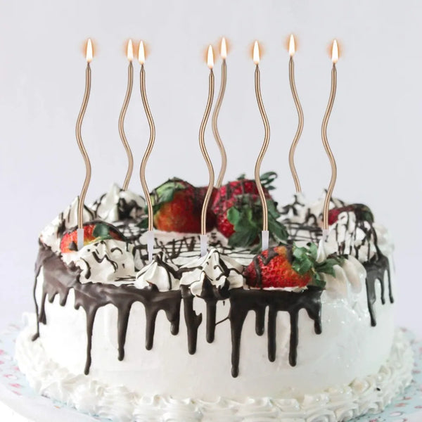 A white cake decorated with chocolate drip and cream frosting, topped with several tall, thin candles.