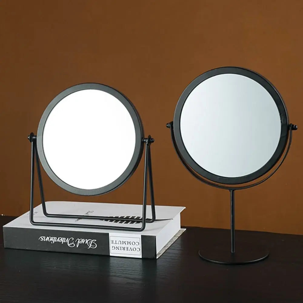 A circular metal makeup mirror with a stand is displayed against a brown background.