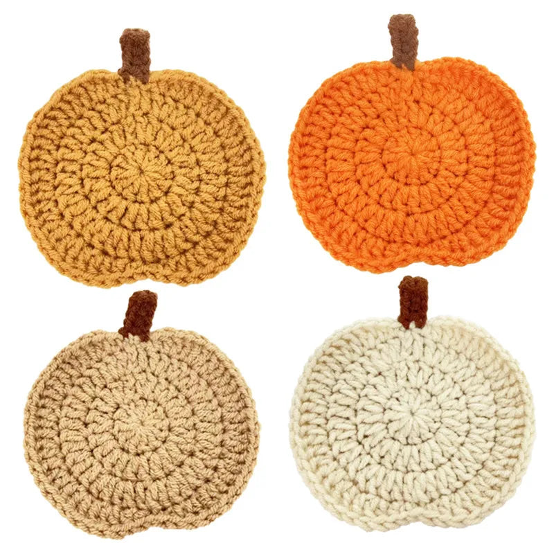 A set of four crocheted pumpkin coasters in various earthy tones.