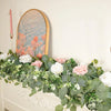 Guirlande artificielle d'eucalyptus avec des fleurs blanches et roses, exposée sur un mur avec une bougie rose.