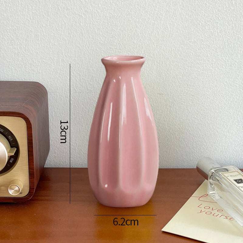 A pink ceramic bud vase with a smooth, rounded shape sits on a wooden surface.