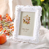 White embossed resin photo frame with a floral design displayed on a light fabric.