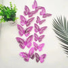 A set of twelve pink and purple 3D butterfly wall stickers displayed on a white surface next to a potted green plant.