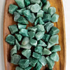 A pile of raw green aventurine crystal stones on a wooden surface.