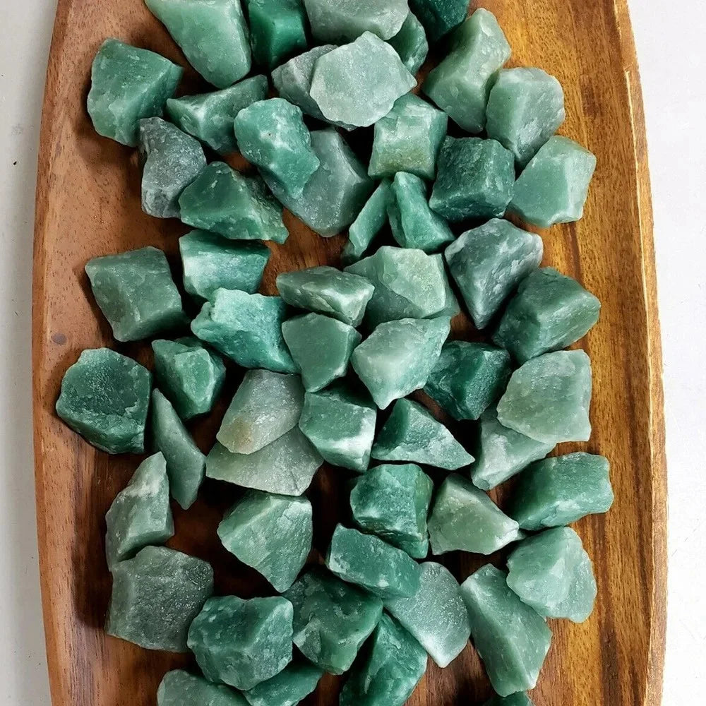 A pile of raw green aventurine crystal stones on a wooden surface.