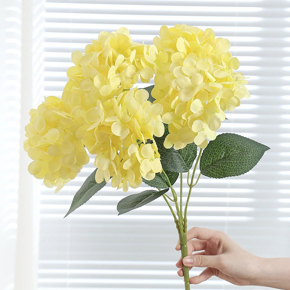 A bouquet of bright yellow artificial hydrangea silk flowers with green leaves.