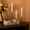 Three tall, slender candles in glass holders with green accents on a dark surface.