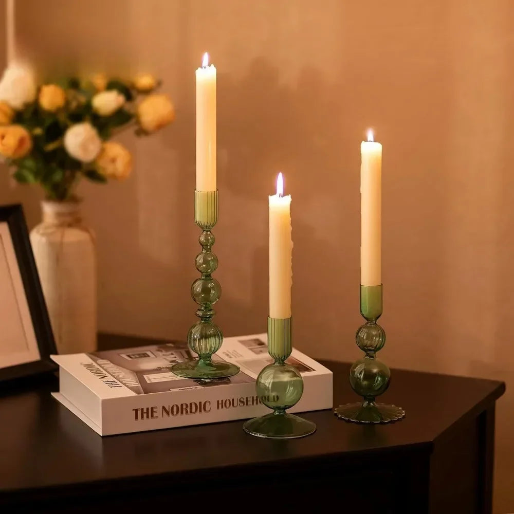 Three tall, slender candles in glass holders with green accents on a dark surface.