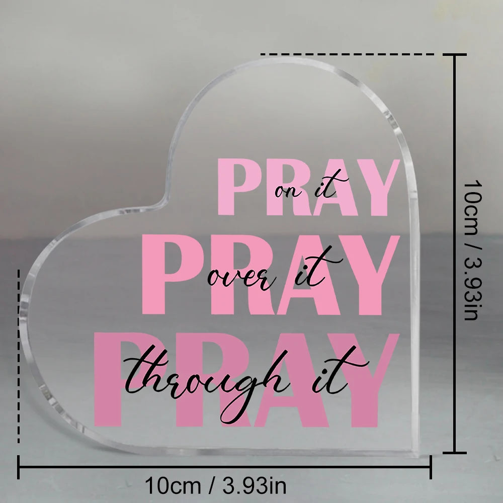 A clear acrylic heart-shaped sign with the text Pray on it Pray over it and Pray through it printed in pink script.
