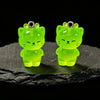 A pair of bright neon green glow-in-the-dark resin charms shaped like a cat and a duck resting on a dark surface.