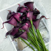 A bouquet of six deep purple artificial calla lilies arranged on white paper