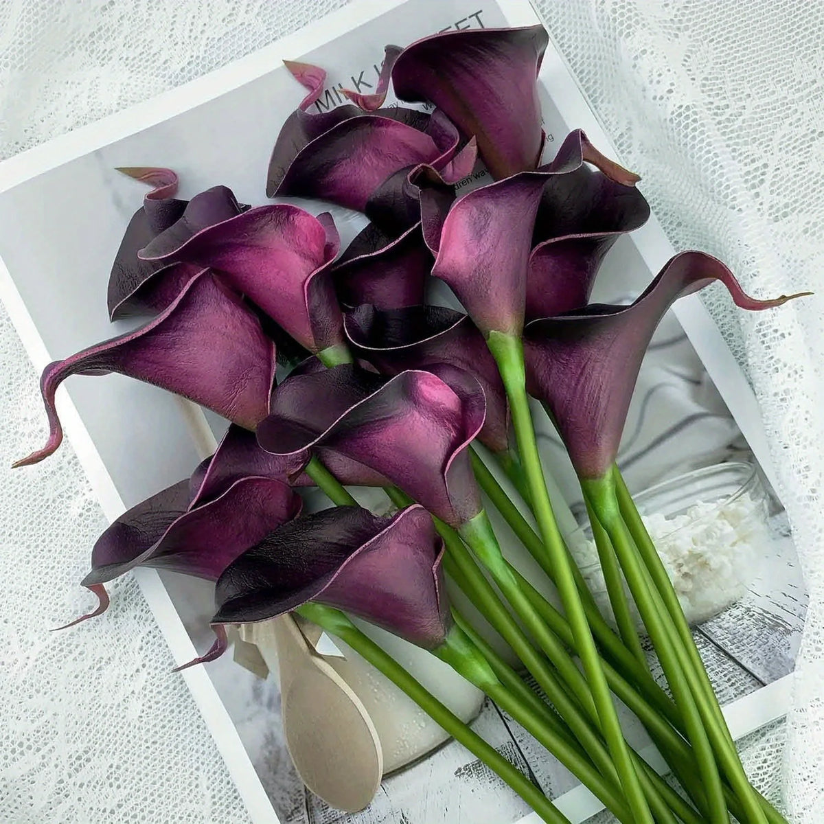 A bouquet of six deep purple artificial calla lilies arranged on white paper