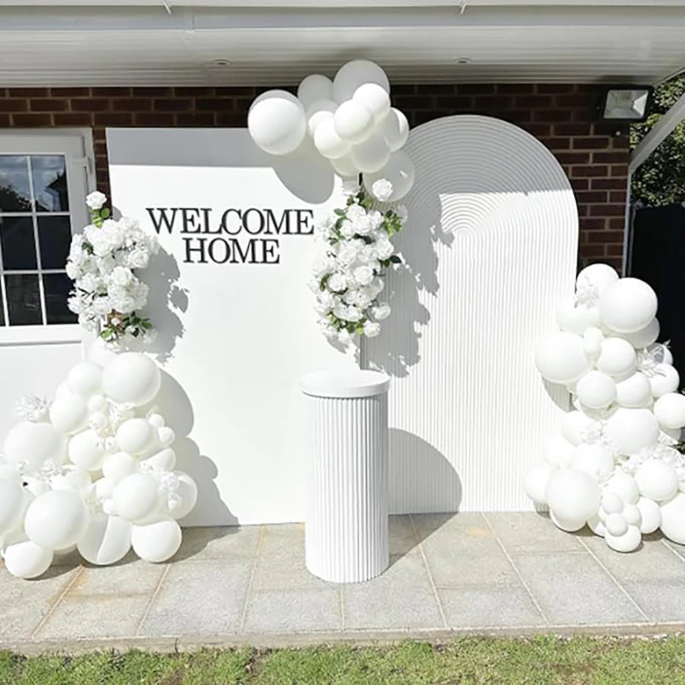 A welcome home decoration featuring white balloons and floral arrangements against a brick wall.