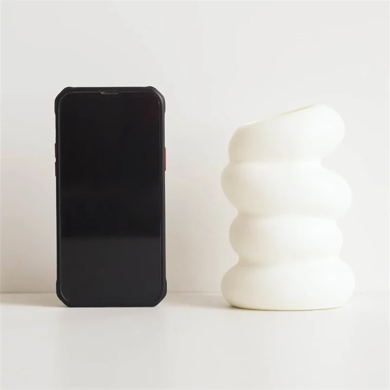A black smartphone next to a white, spiral-shaped decorative vase.