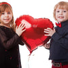 Two young children holding a large red heart foil balloon for Valentine's Day decorations