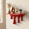 A red drip floating shelf displaying dried grasses, a wooden object, and a small potted succulent on a white wall.