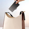A beige vanity mirror is being held over a light tan leather handbag.