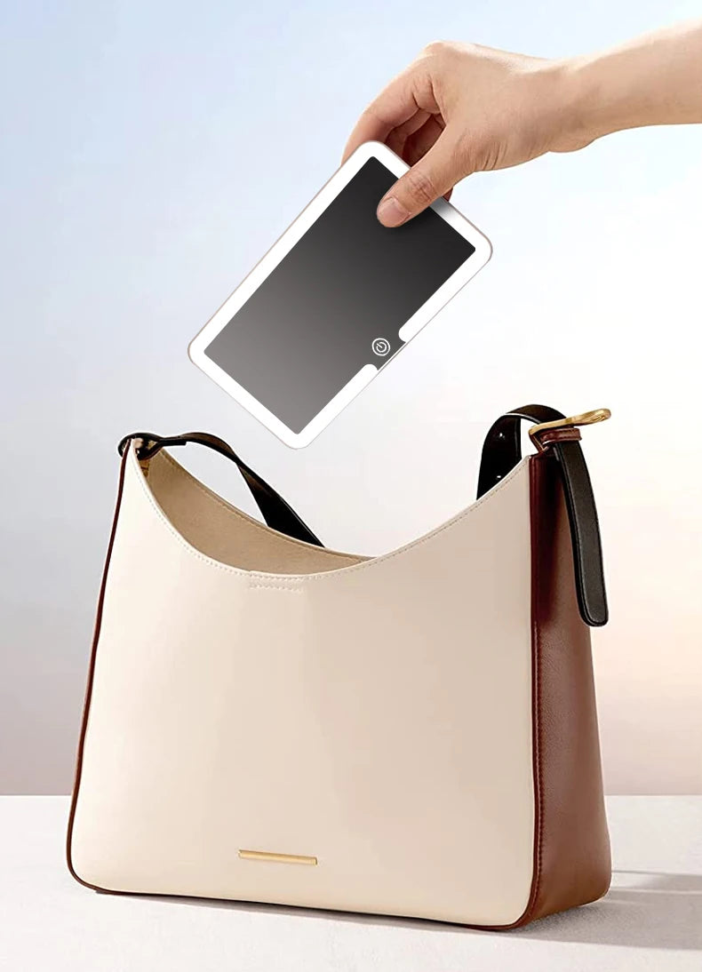 A beige vanity mirror is being held over a light tan leather handbag.