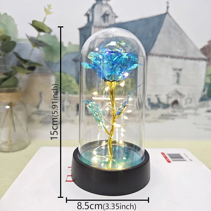 A glass dome featuring an eternal blue rose with a golden stem and LED light, displayed on a white surface.